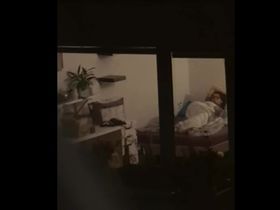 Девушка лежит под одеялом и мастурбирует пока парень снимает ее на камеру через окно