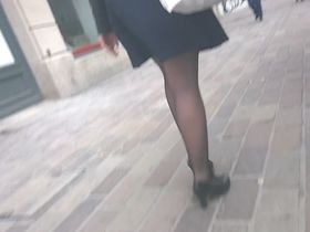 Женщина с красивыми ножками в черных колготках прогуливается по городу